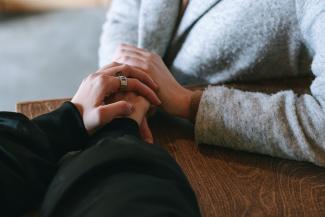 The hands of two people who care about each other and are sitting at a wooden table.