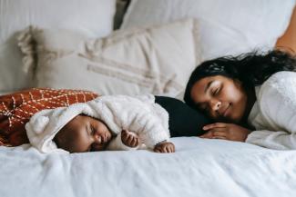 A mother naps with her newborn in a cozy bed. 