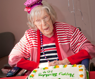 An older woman celebrates her 104th birthday. A cake is in front of her and a present is behind her.