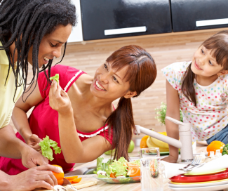 A mother and father make a salad with their young daughter watching.